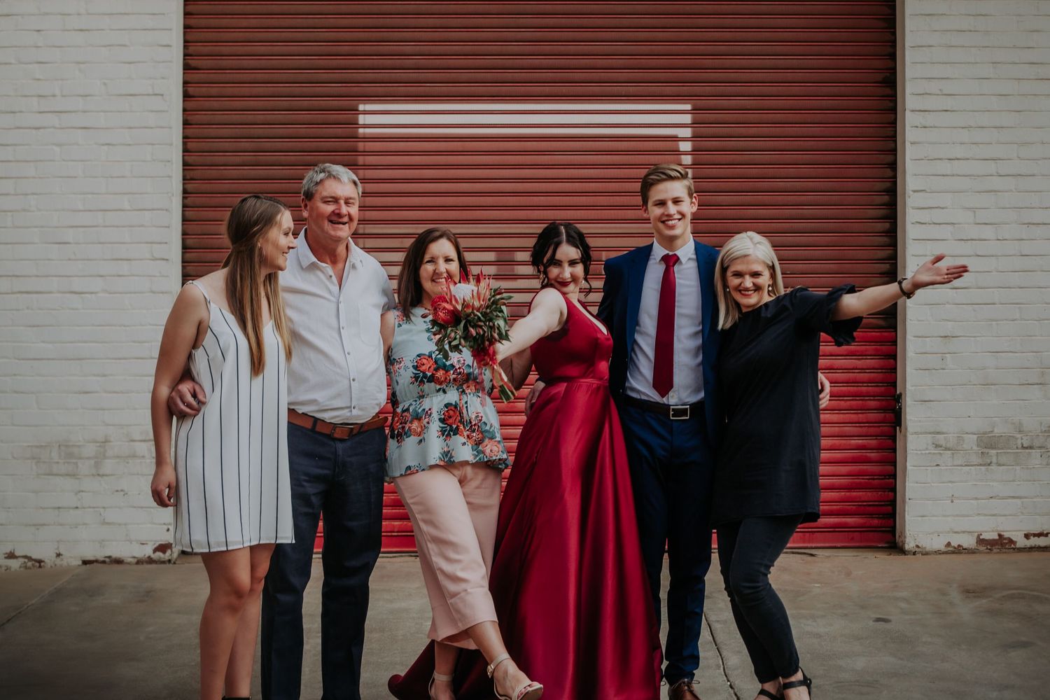 A celebratory group photo with friends posing casually against a red garage door.