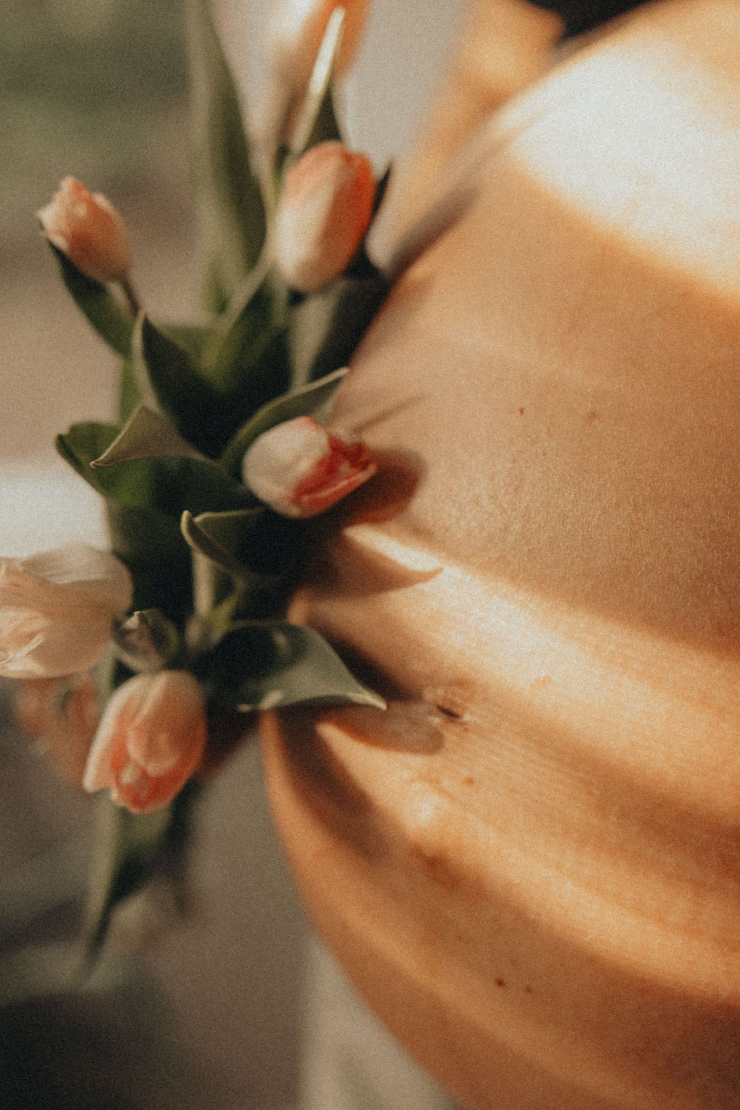 Pregnant woman's bare baby bump adorned with soft pink tulips in warm sunlight, creating a serene maternity moment.