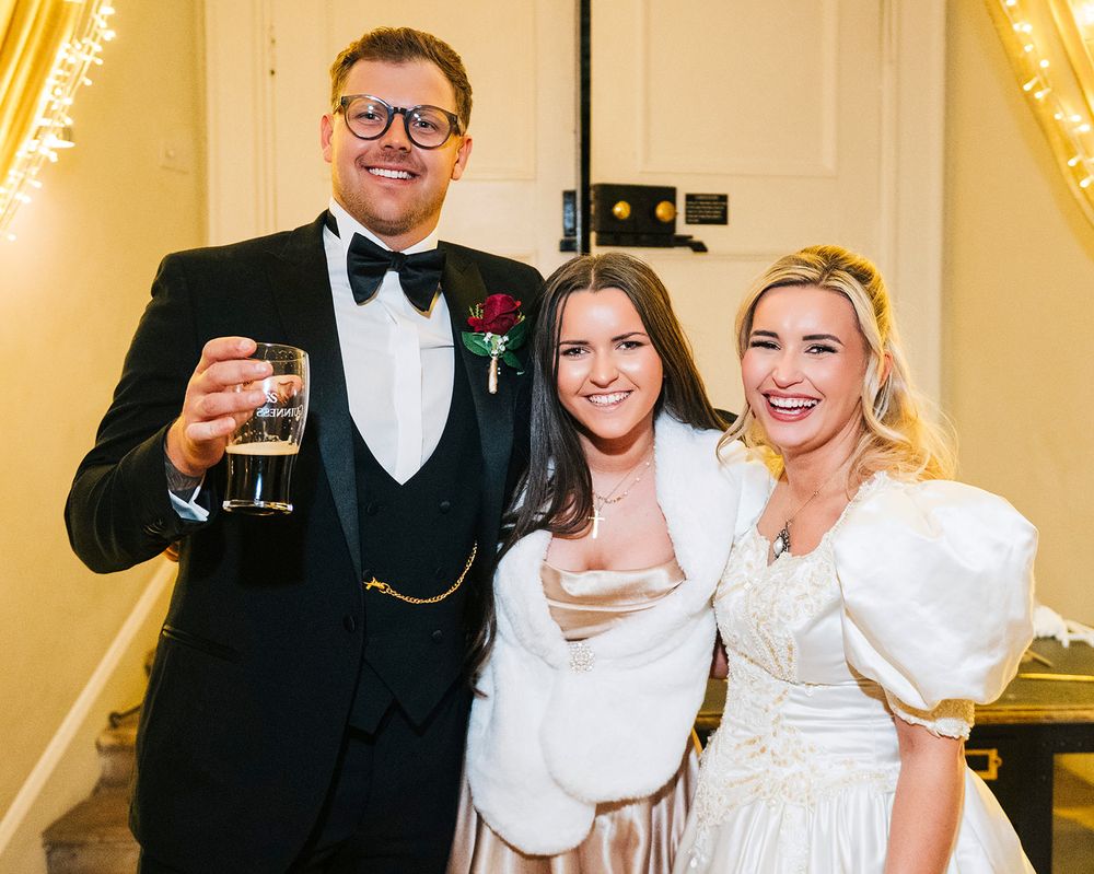 A group of people in formal white attire pose together at an elegant indoor event.