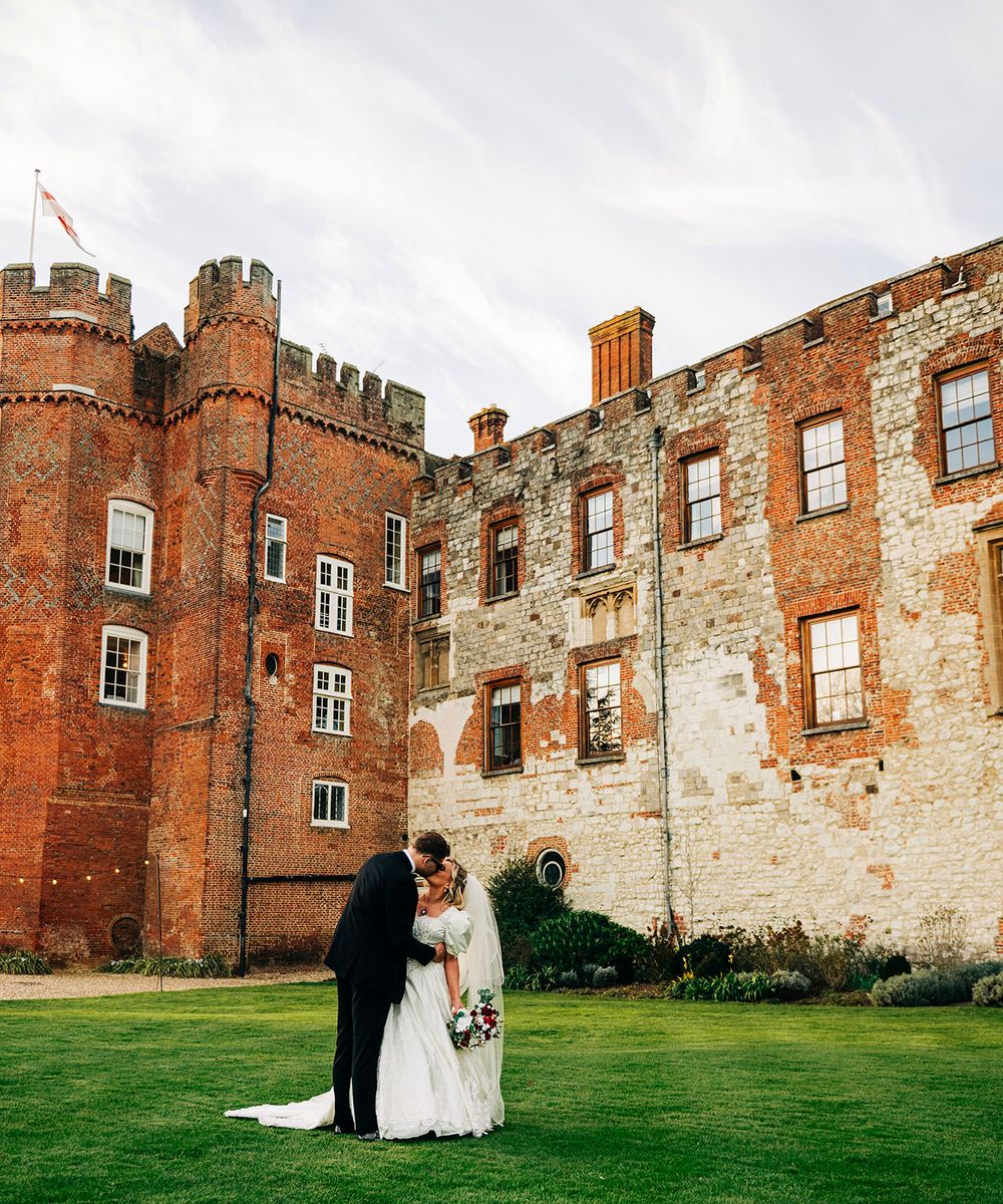 A couple walks along the stone walls of a historic brick castle courtyard during a wedding photo session.