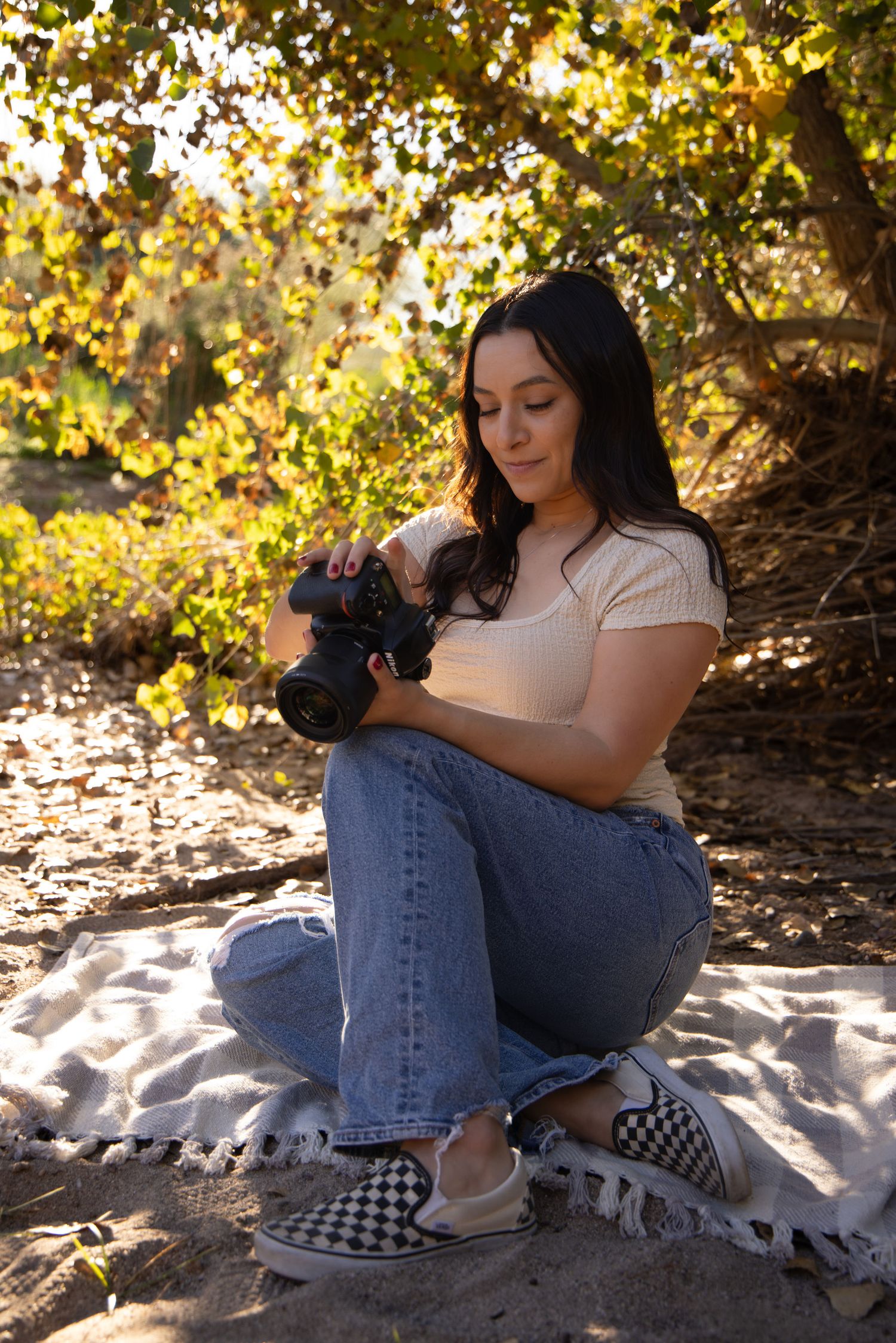 Casual outdoor photoshoot on white blanket with denim and checkered shoes against autumn foliage.