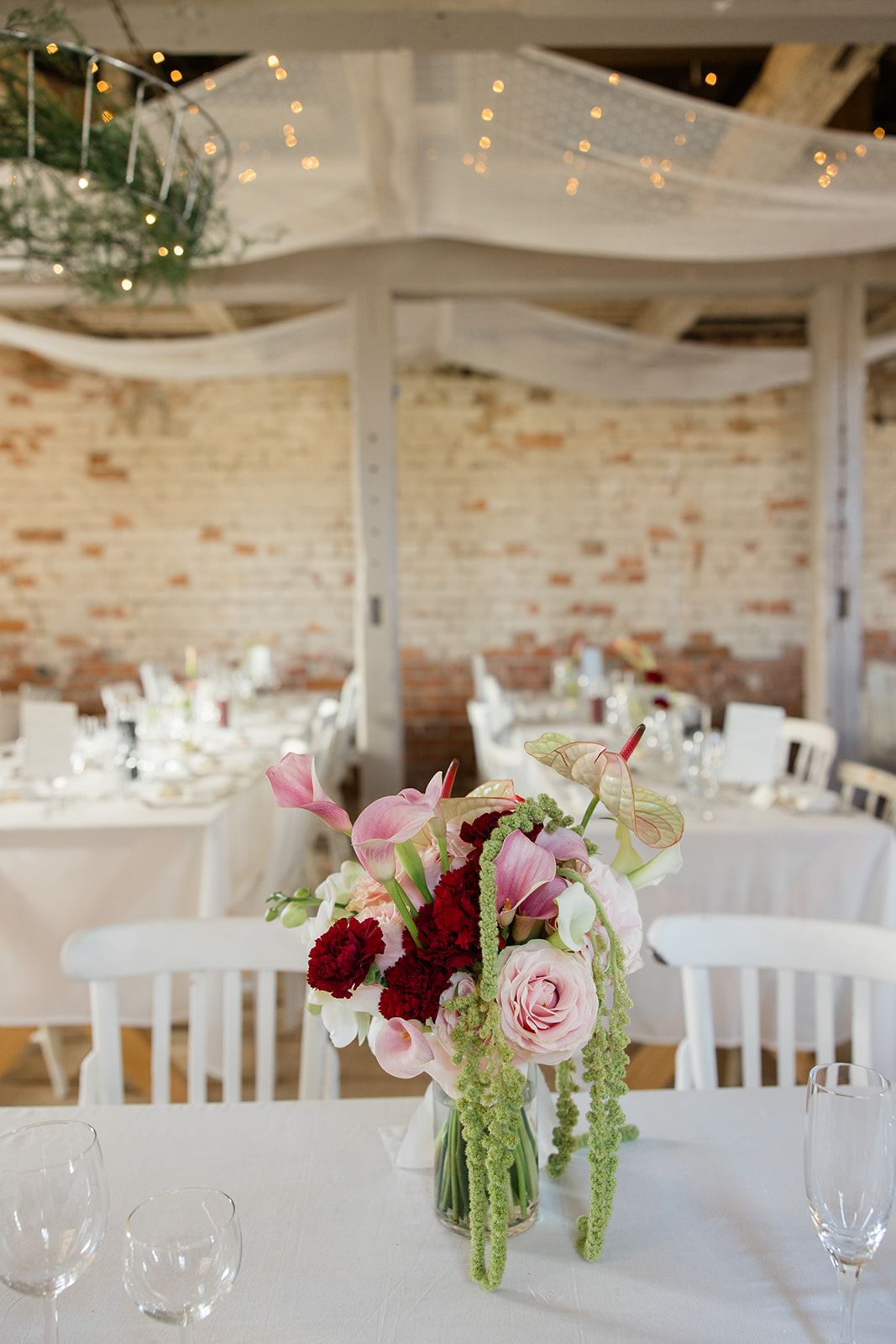 Elegant wedding reception venue with exposed brick walls, white chairs, and pink floral centerpieces on round tables.