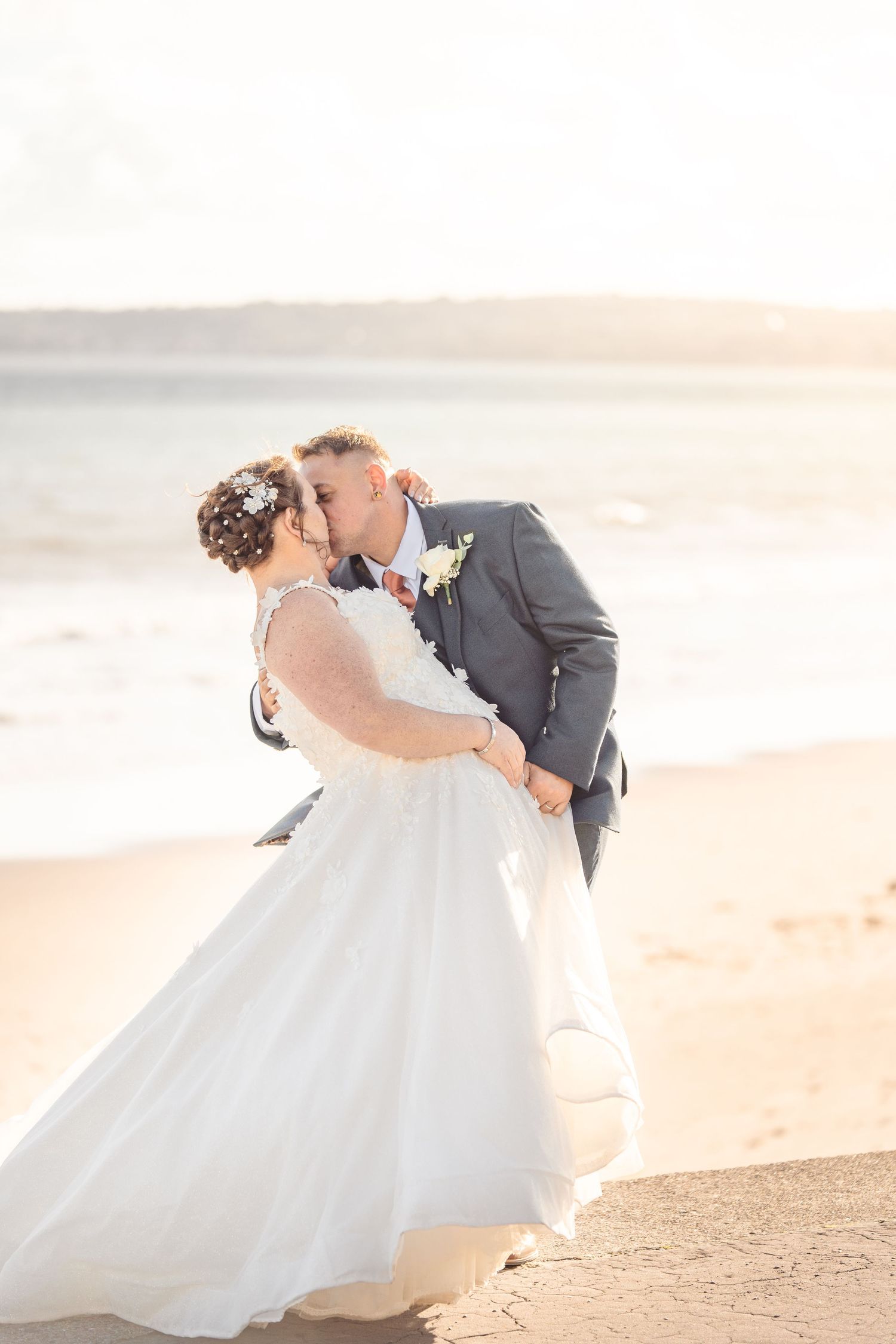 Romantic wedding couple embraces on a sandy beach at sunset in a dreamy coastal setting.