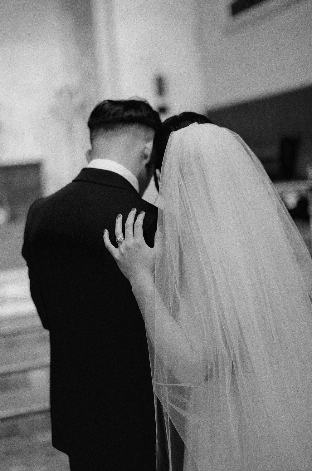 A timeless black and white film portrait of the couple embracing near the chancel, emphasizing the low-light of the Santa Barbara chapel.