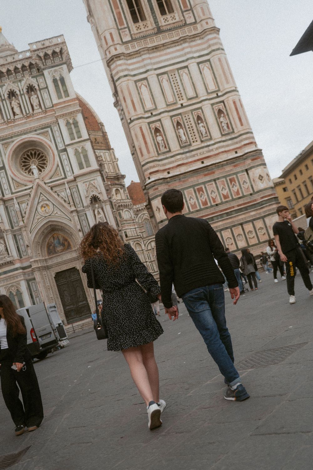 Two people walk hand in hand in front of Florence's iconic Duomo cathedral.