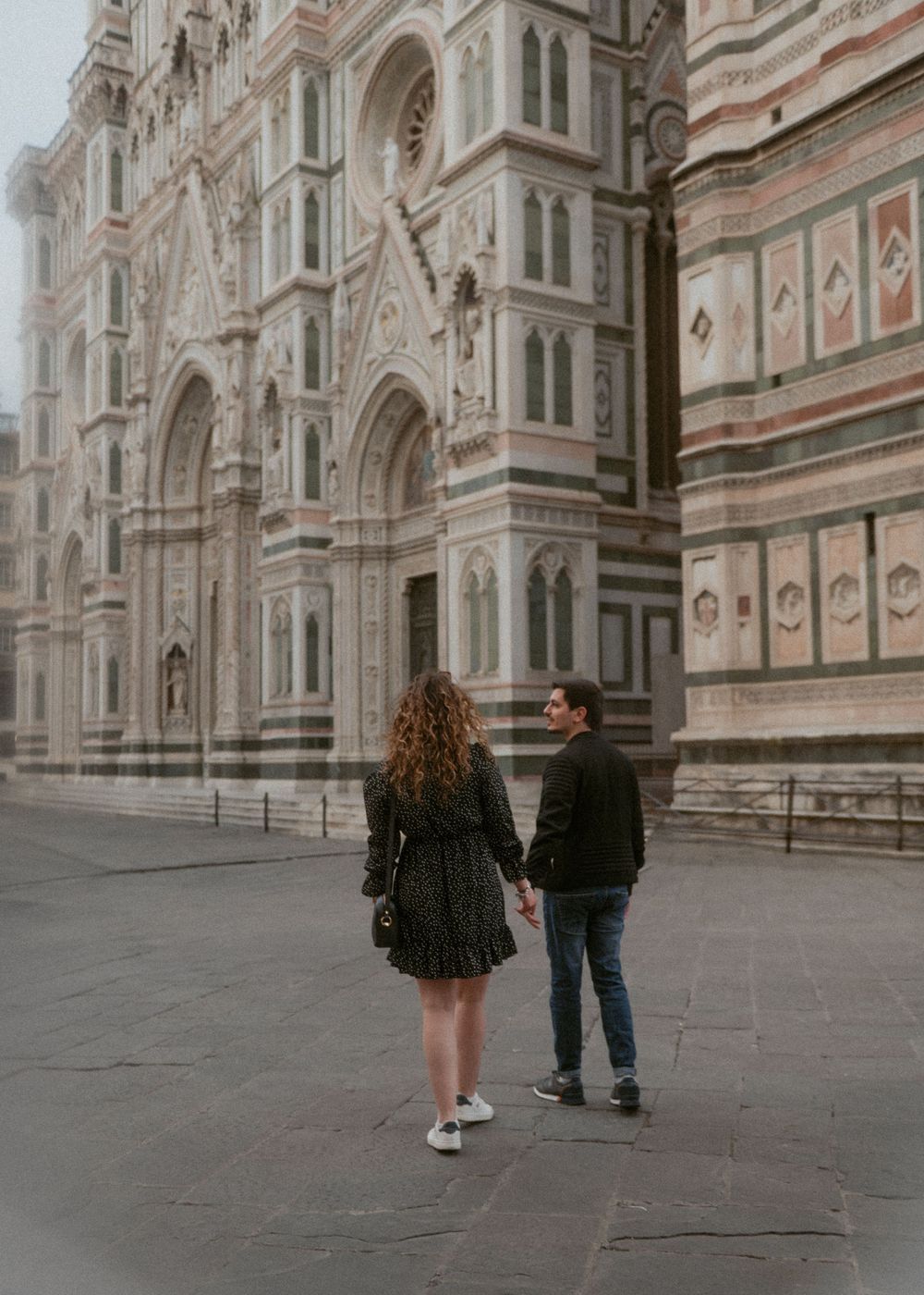 A couple walking hand in hand outside the ornate facade of Florence's Duomo cathedral.