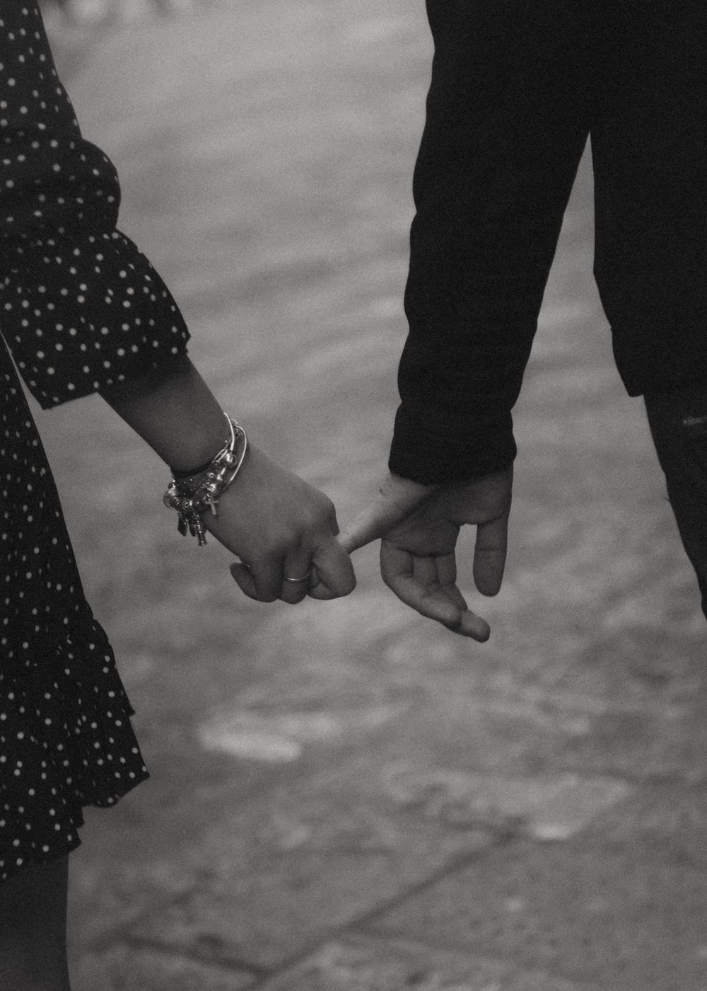 A black and white close-up of two people holding hands, with one wearing a polka dot dress.
