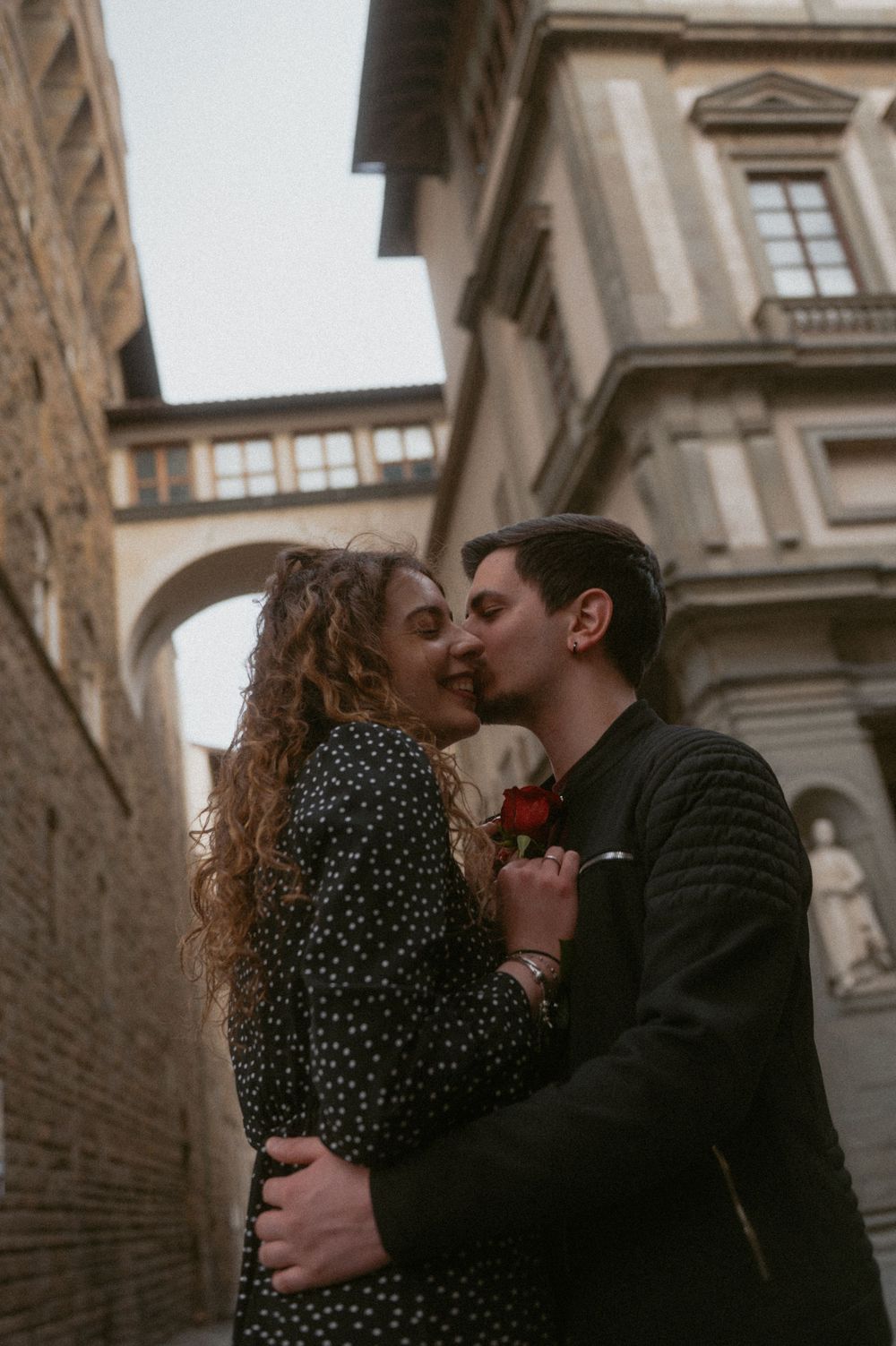 A couple embraces in a tender moment against a stone building backdrop.