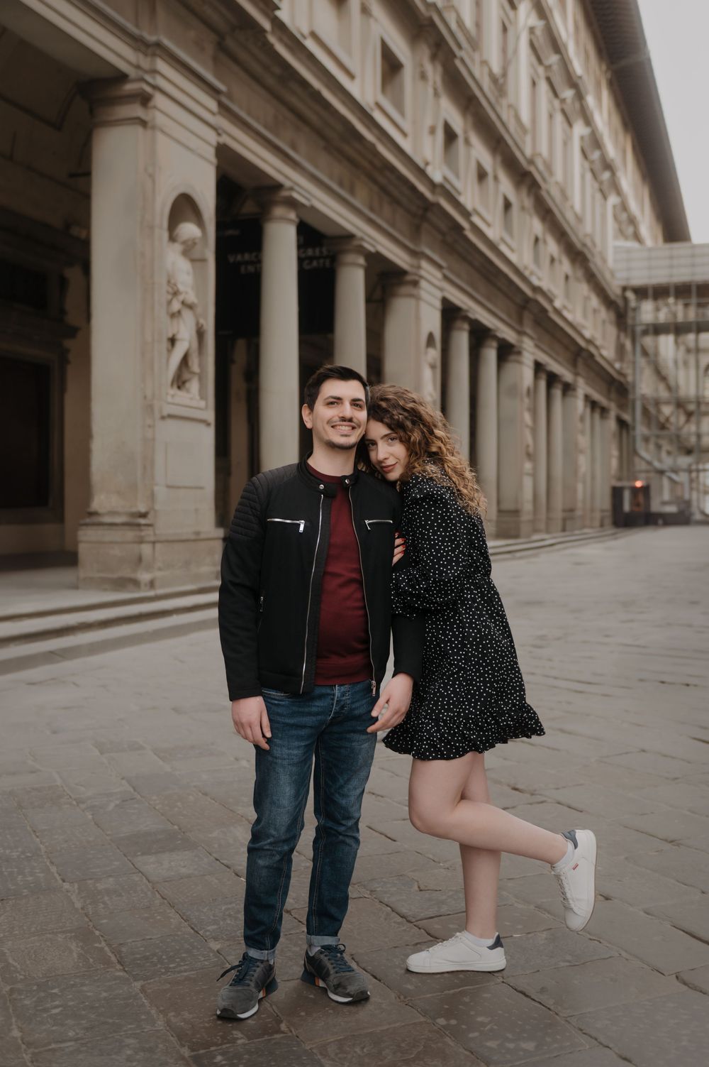 A romantic couple poses in front of ornate classical architecture with columns in Florence, Italy.