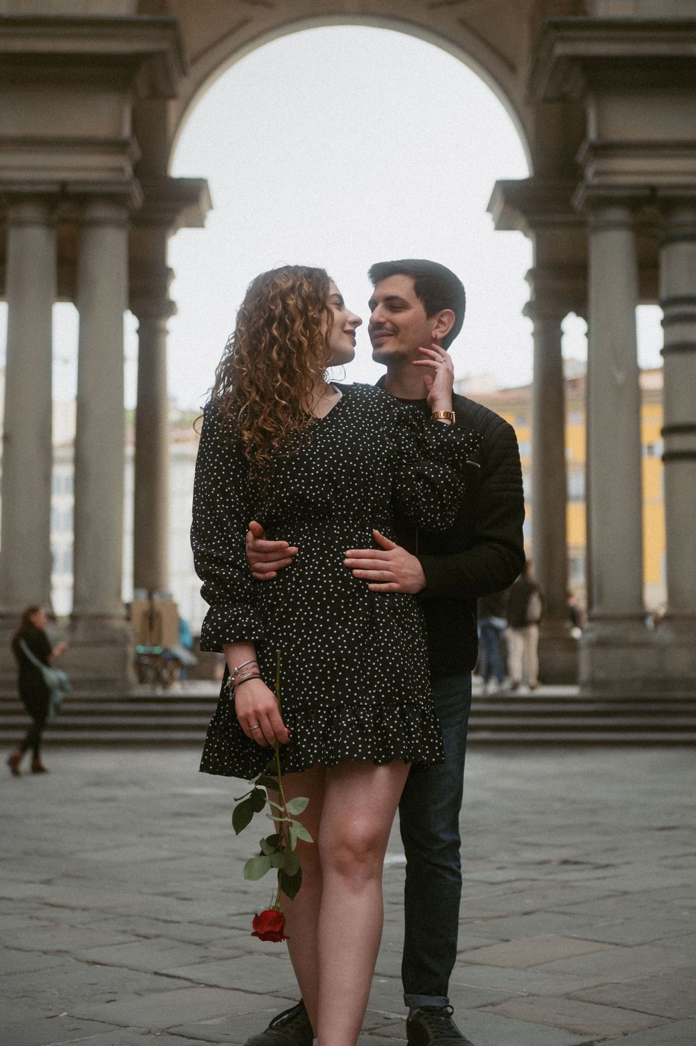 A couple shares a romantic dance under an ornate Italian colonnade with a rose.