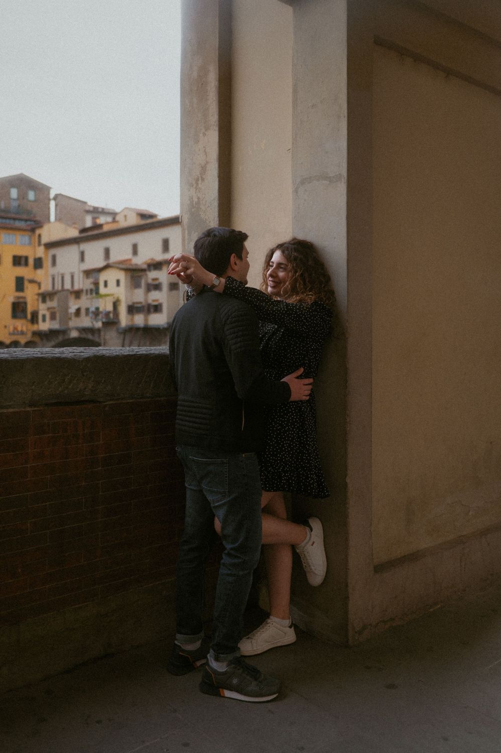 A couple shares an intimate moment in a dimly lit archway of an urban building.