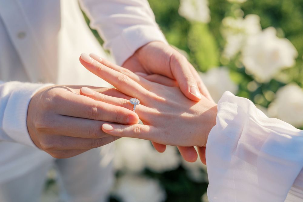 Close-up sequence showing hands exchanging wedding rings during an outdoor ceremony with blurred floral background.