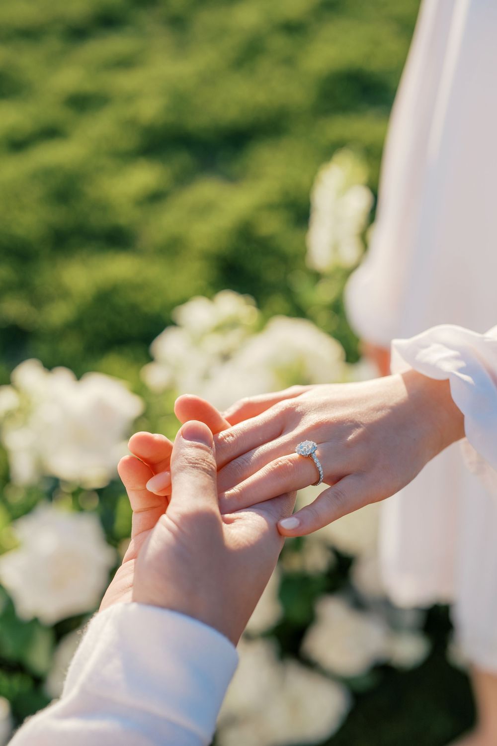 Close-up view of hands exchanging wedding rings against a blurred floral background.