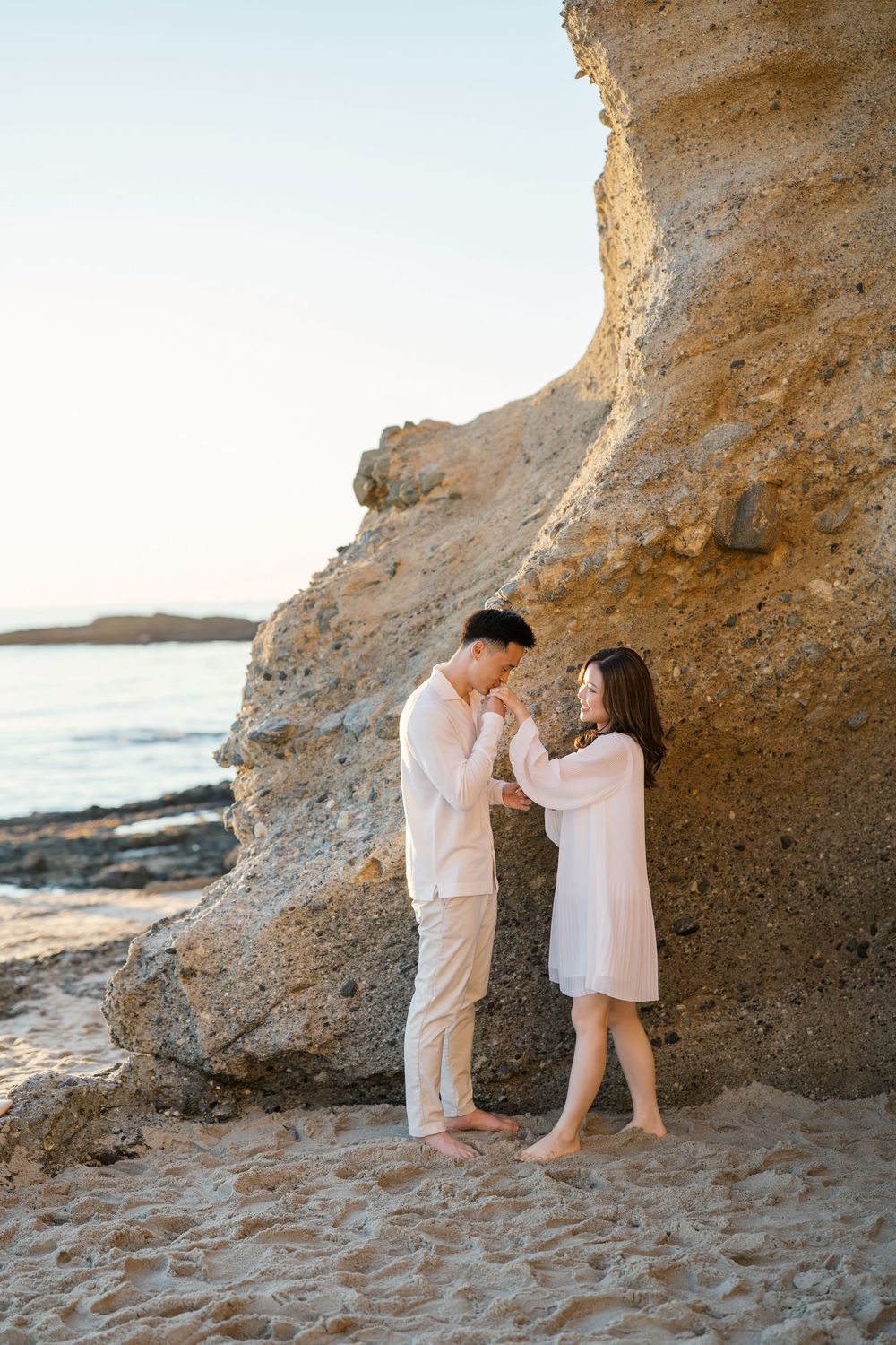 A romantic beach photoshoot at sunset with a couple posing near limestone cliffs by the ocean.