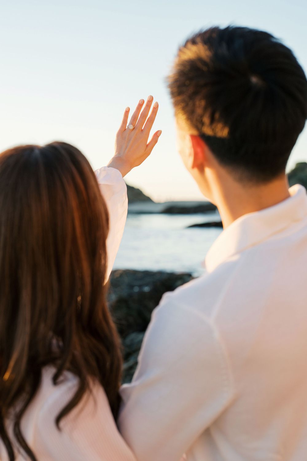 A group of people in white clothing wave goodbye while standing at a scenic overlook during sunset.