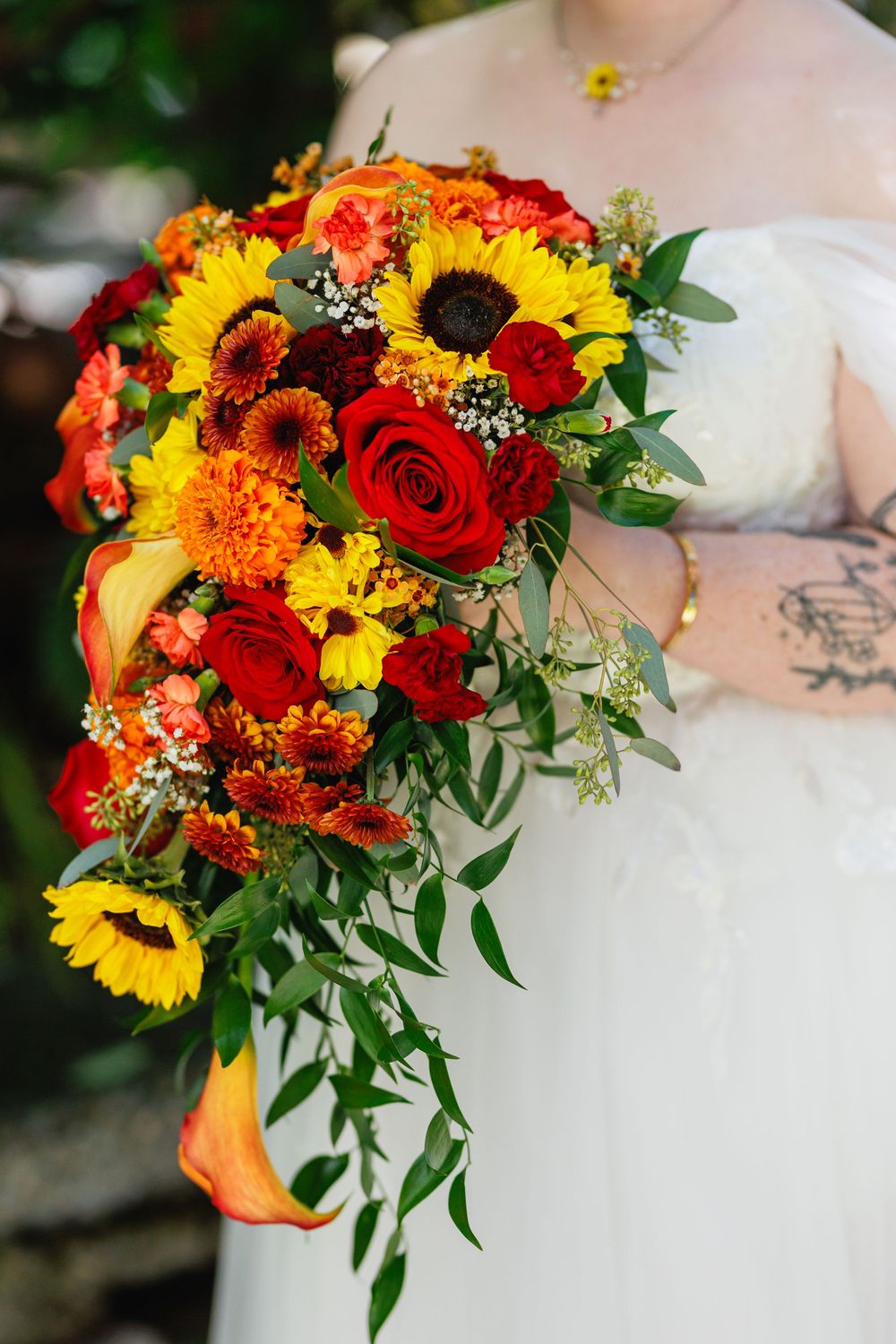Close-up of a cascading bridal bouquet featuring sunflowers, red roses, and orange blooms with greenery.