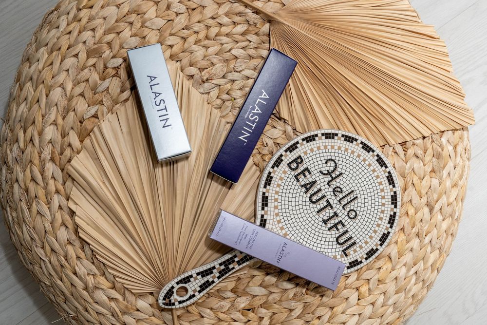 Straw sun hat with beauty product samples and cosmetic bottles arranged on top against white background.