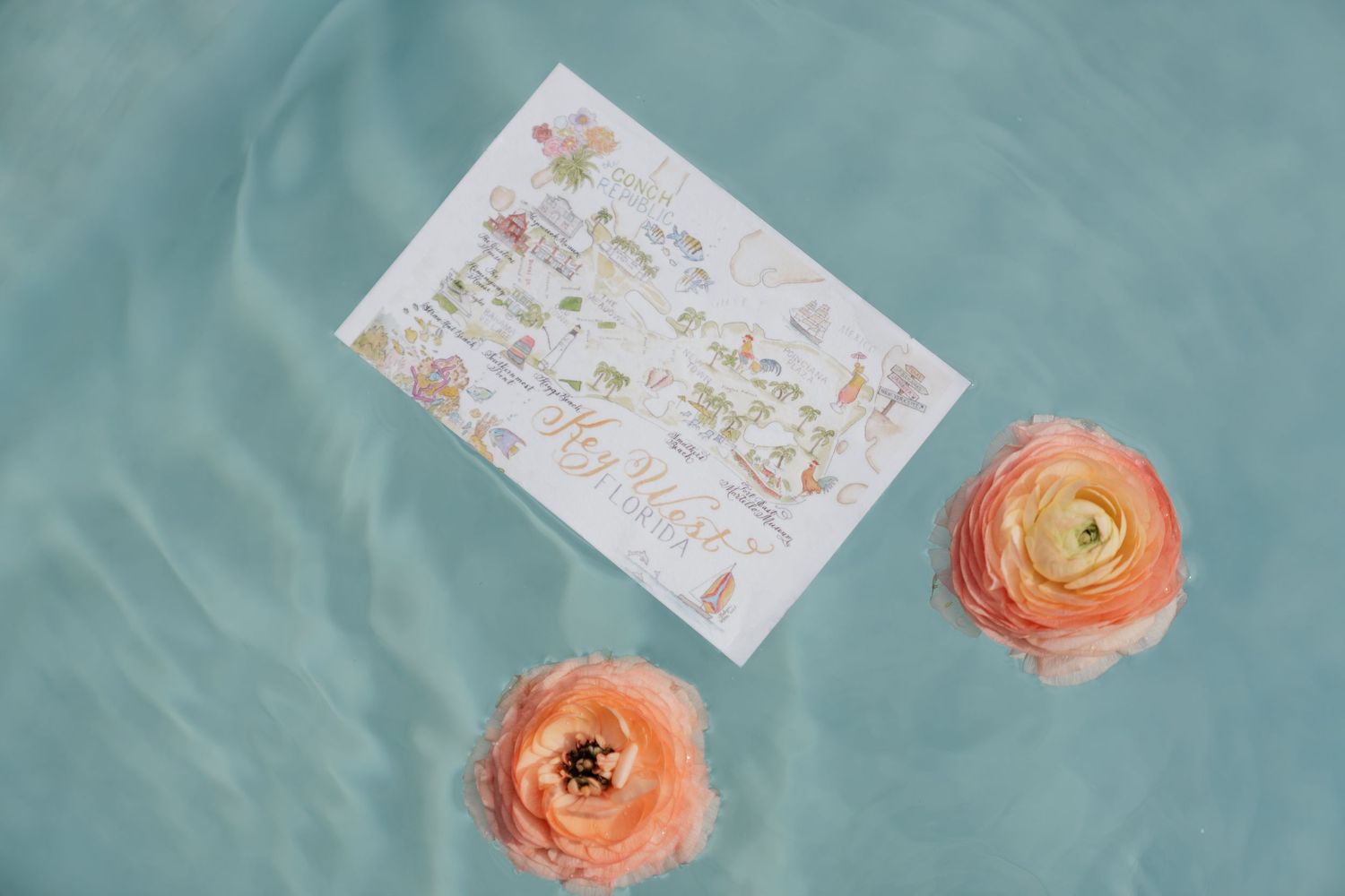 Peach-colored ranunculus flowers and delicate handwritten notes arranged on a soft turquoise background.