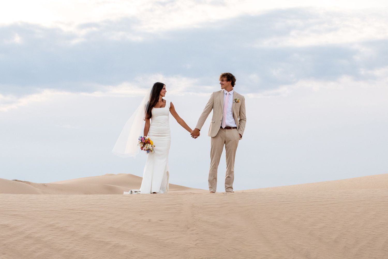 Bride and groom poses together on sandy dunes at sunset during desert wedding photo session in Utah.