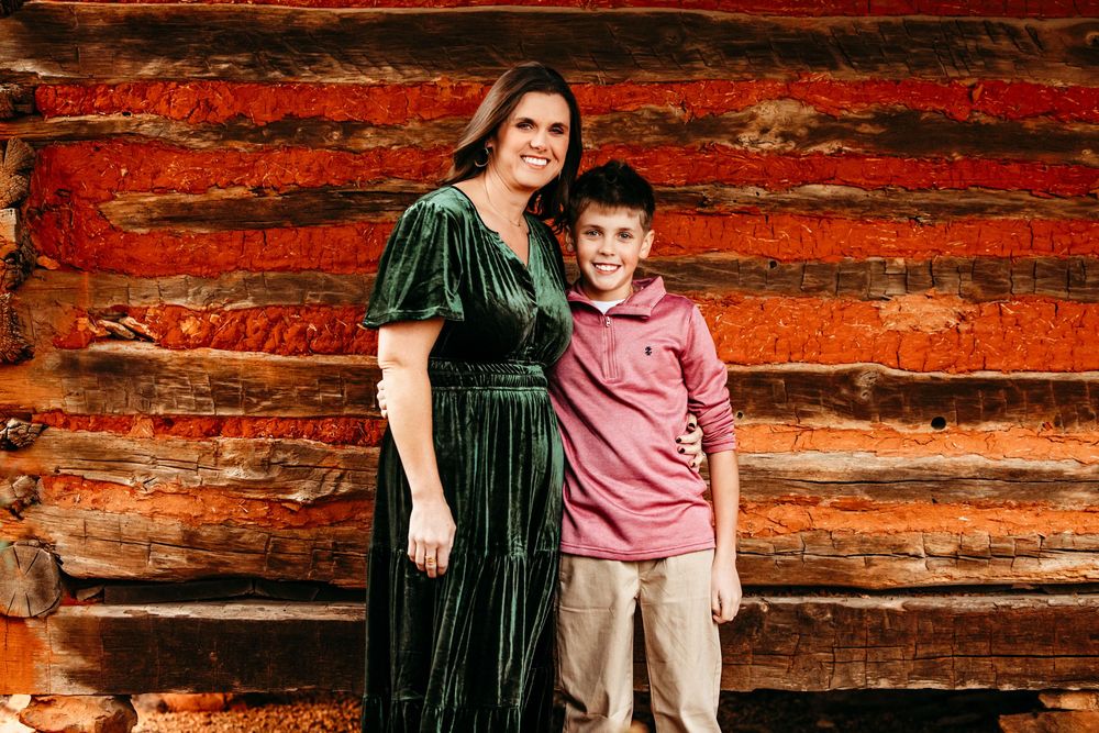 Family members pose together against rustic red wooden wall backdrop in coordinated casual outfits.