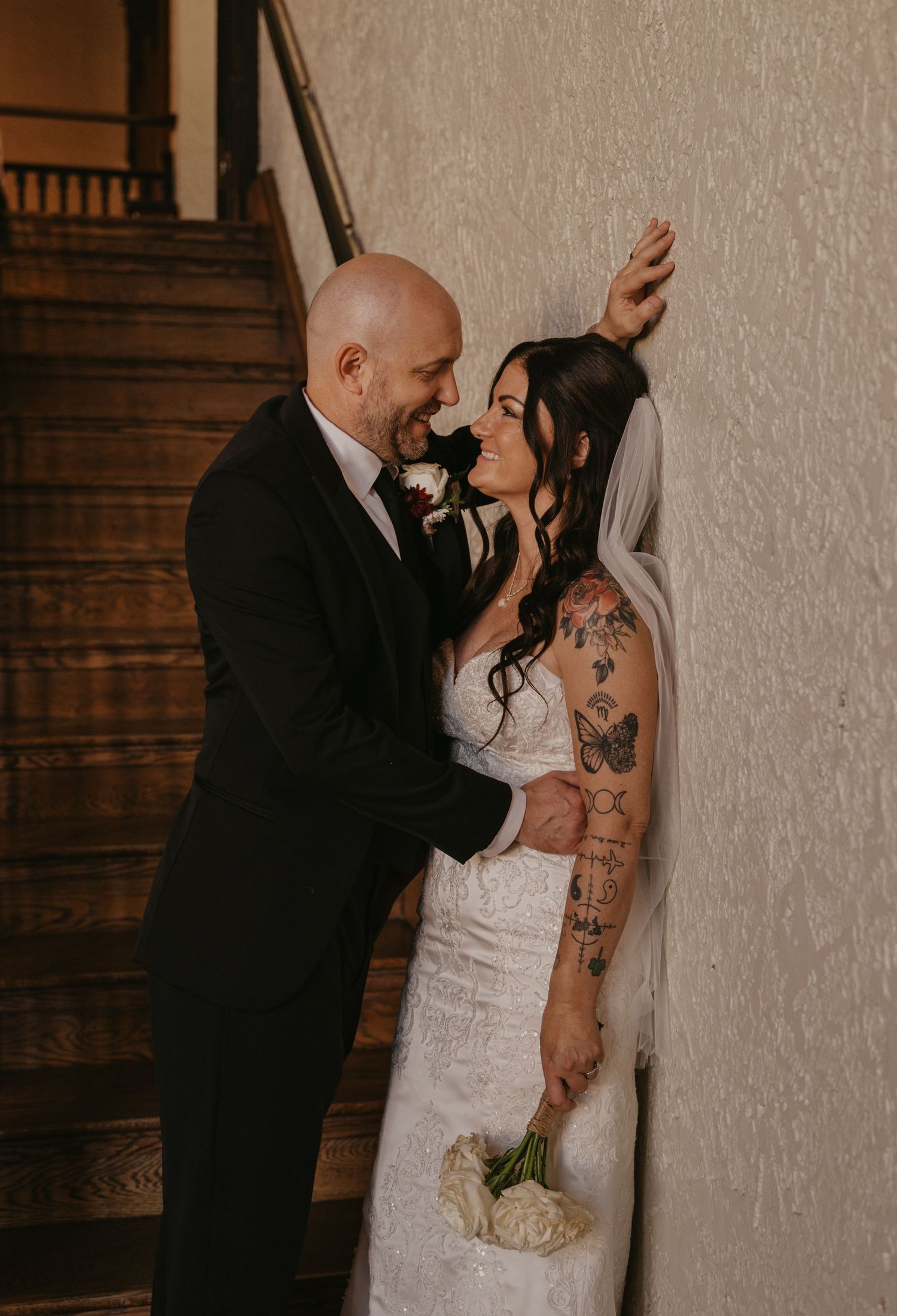 A romantic wedding couple shares an intimate moment against a rustic wooden wall and staircase.
