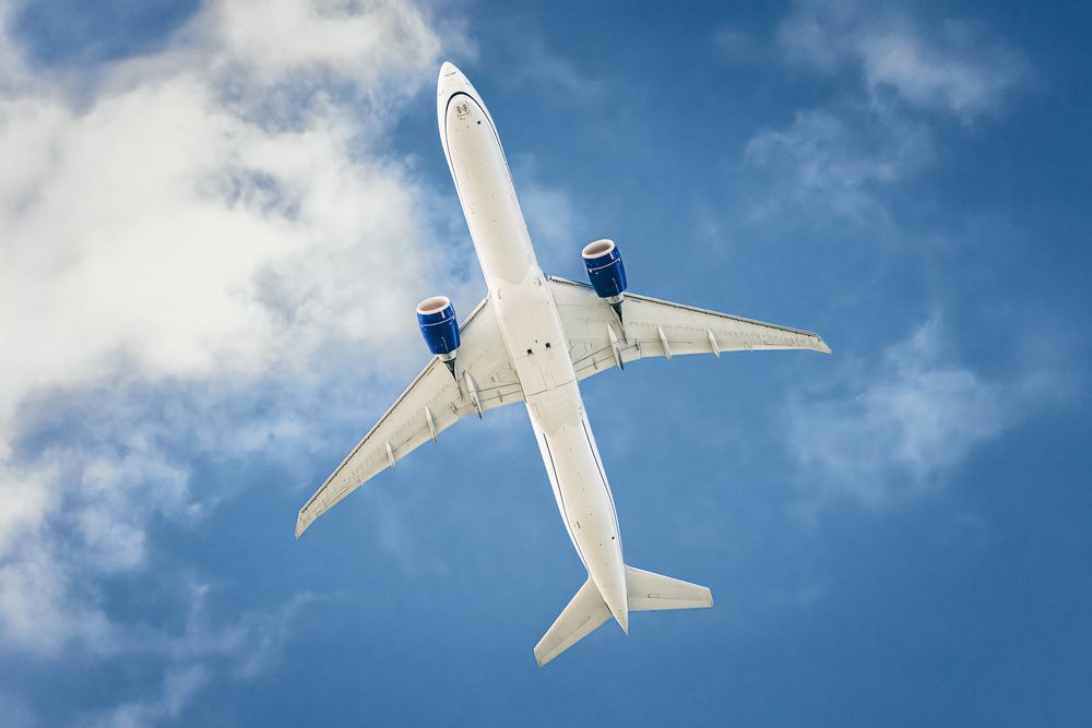 Commercial airplane flying against blue sky with white clouds.
