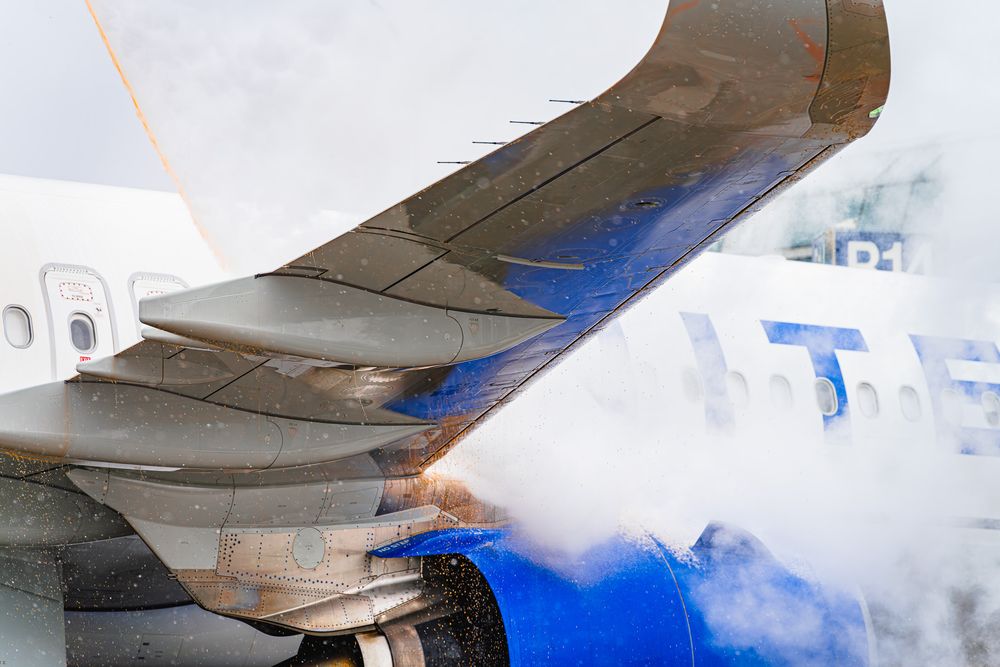 Close-up view of a commercial airplane wing against a cloudy blue sky.