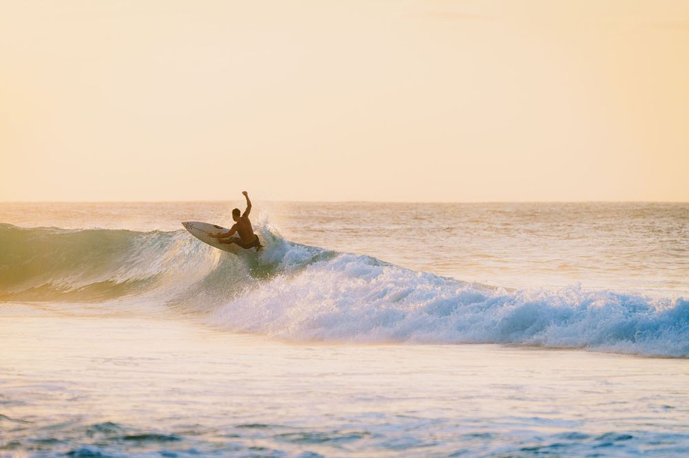 Surfer riding a wave during golden hour with ocean spray.