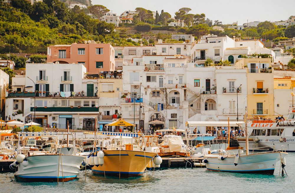 Mediterranean coastal village with colorful boats docked in a harbor surrounded by white buildings.