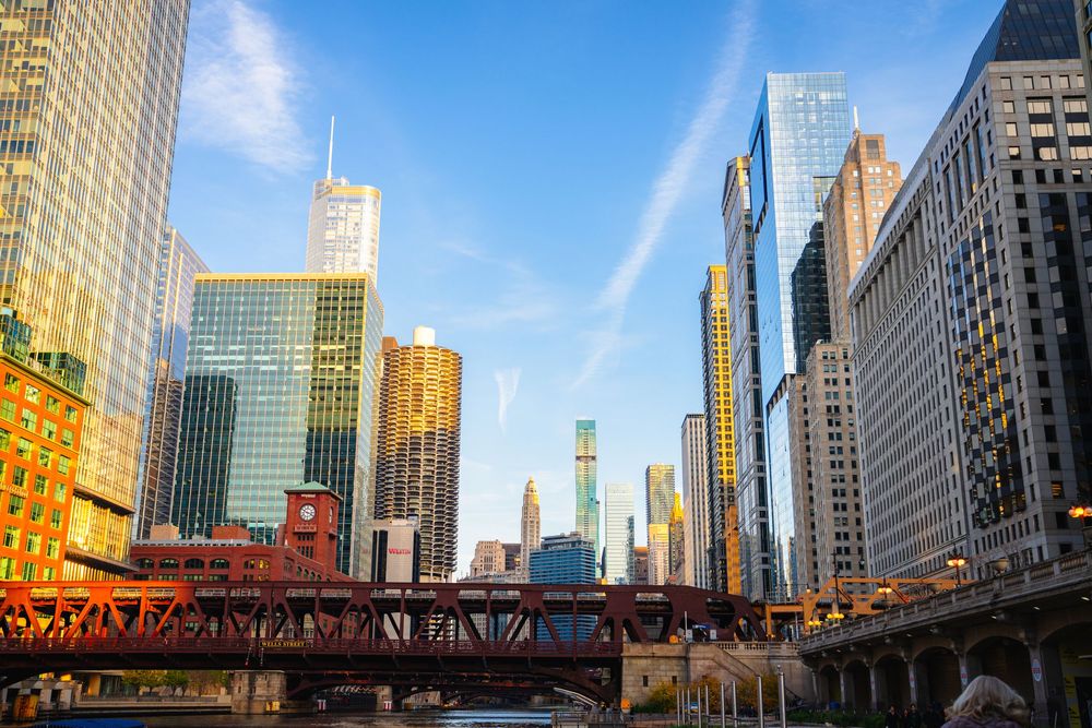 Chicago River flows through downtown with iconic skyscrapers and a red bridge under bright blue skies.
