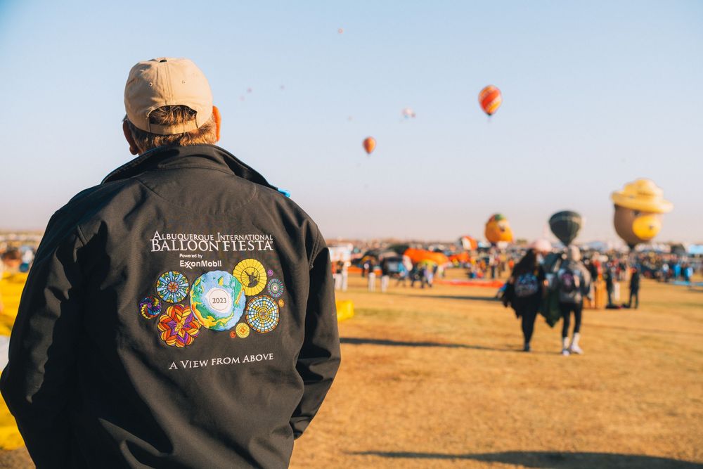 Hot air balloon festival attendee watching colorful balloons launch in field.
