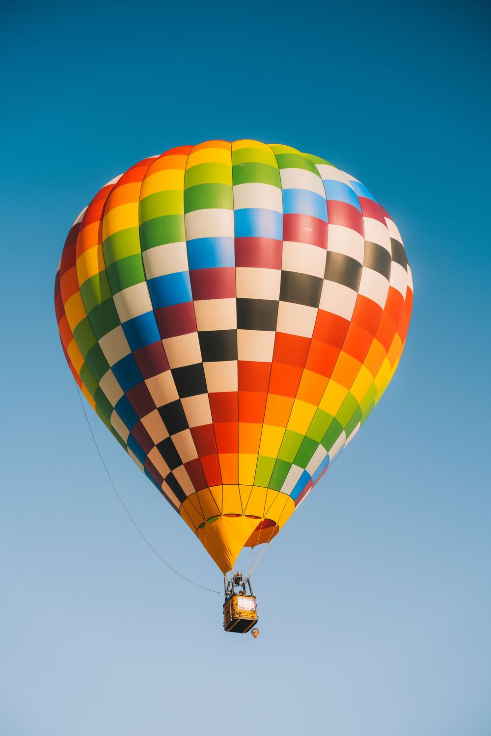 Colorful checkered rainbow hot air balloon floating in clear blue sky.