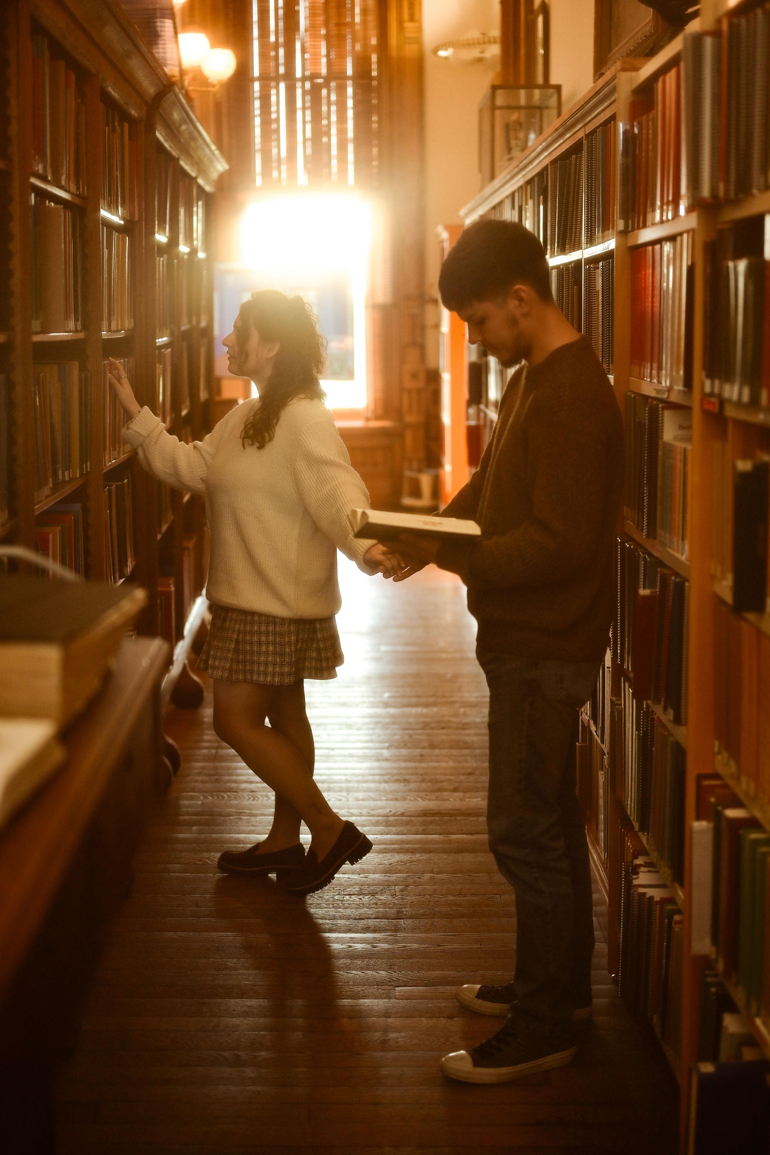Silhouettes of people browsing books in a dimly lit library aisle with warm glowing lights creating an atmospheric mood.