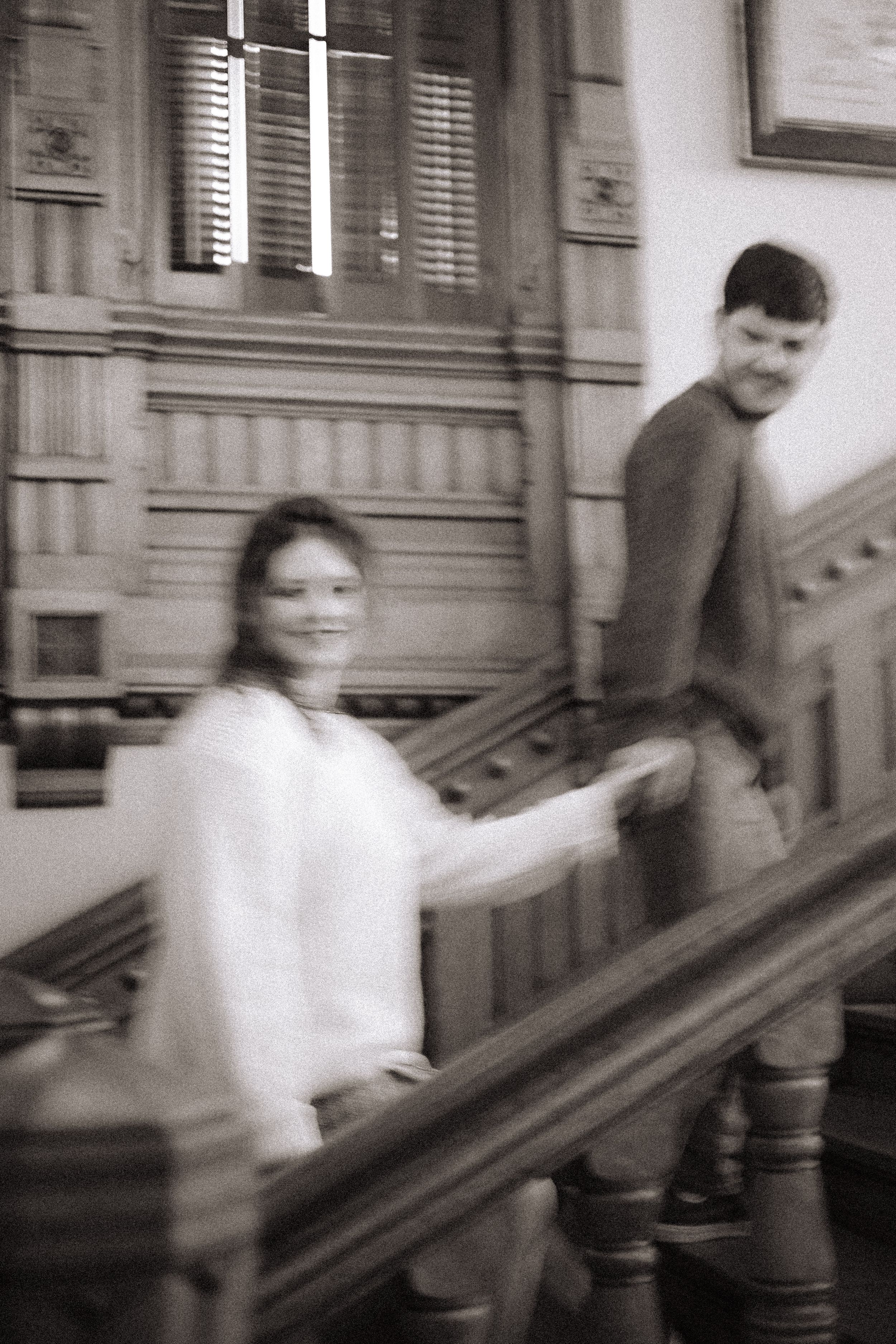 A blurred black and white sequence of motion showing people walking down stairs in a building.