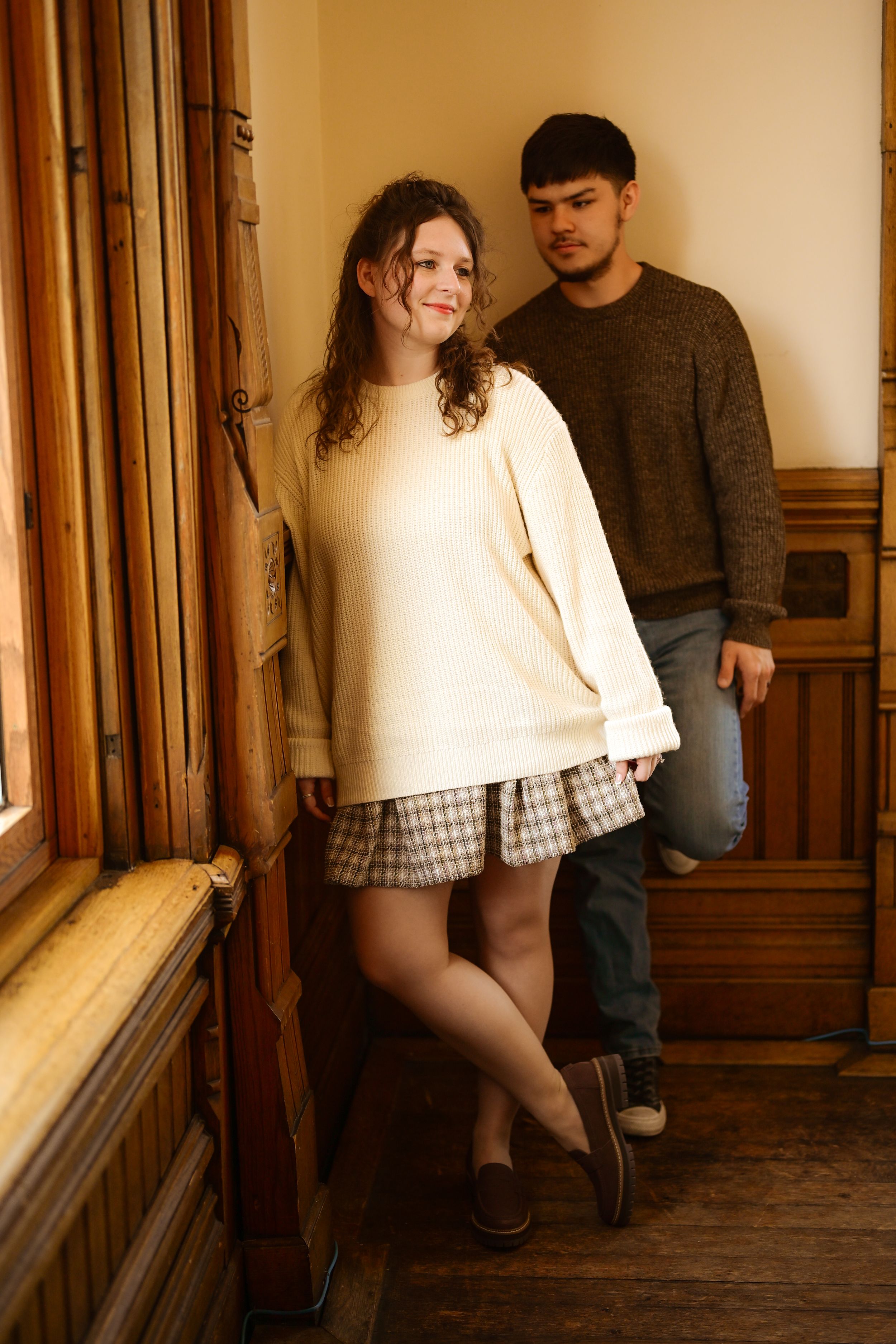 A romantic couple poses together in a vintage hallway with warm lighting and wooden wall panels.