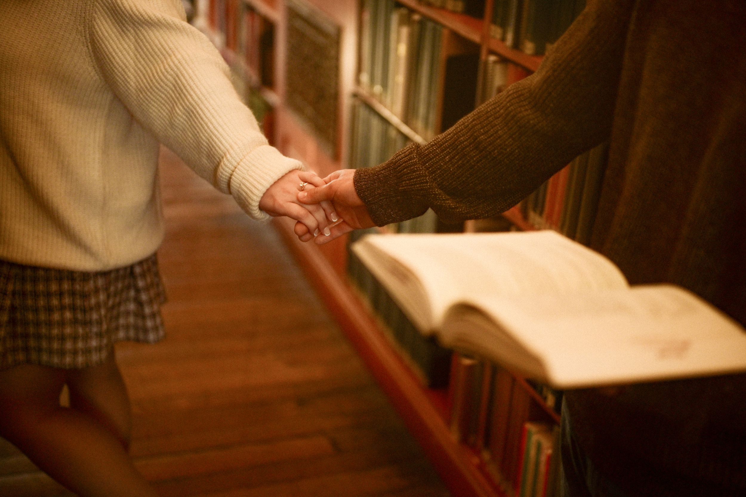 Two people shake hands in a library with bookshelves and an open book in the background.