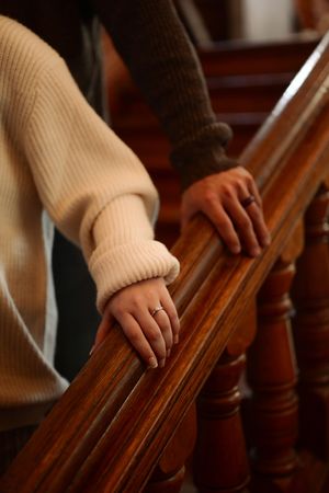 Close-up view of hands sliding down a wooden banister while wearing a beige knit sweater.