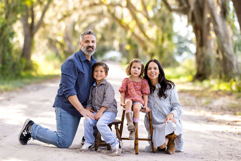 A family group poses together outdoors in casual clothing on a tree-lined path during an autumn photo session.