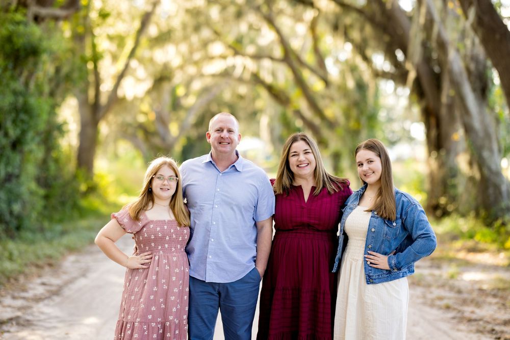 A family poses together outdoors on a tree-lined path during a golden hour photo session.