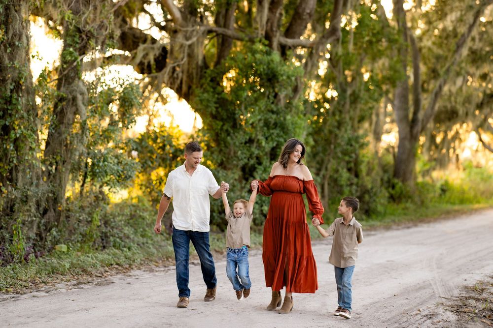 A family walks together on a dirt path surrounded by Spanish moss-draped trees during golden hour.