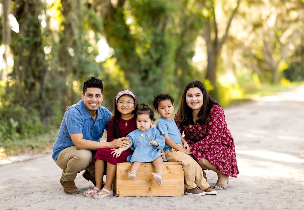A group poses together outdoors on a dirt path surrounded by greenery in matching burgundy and blue outfits.