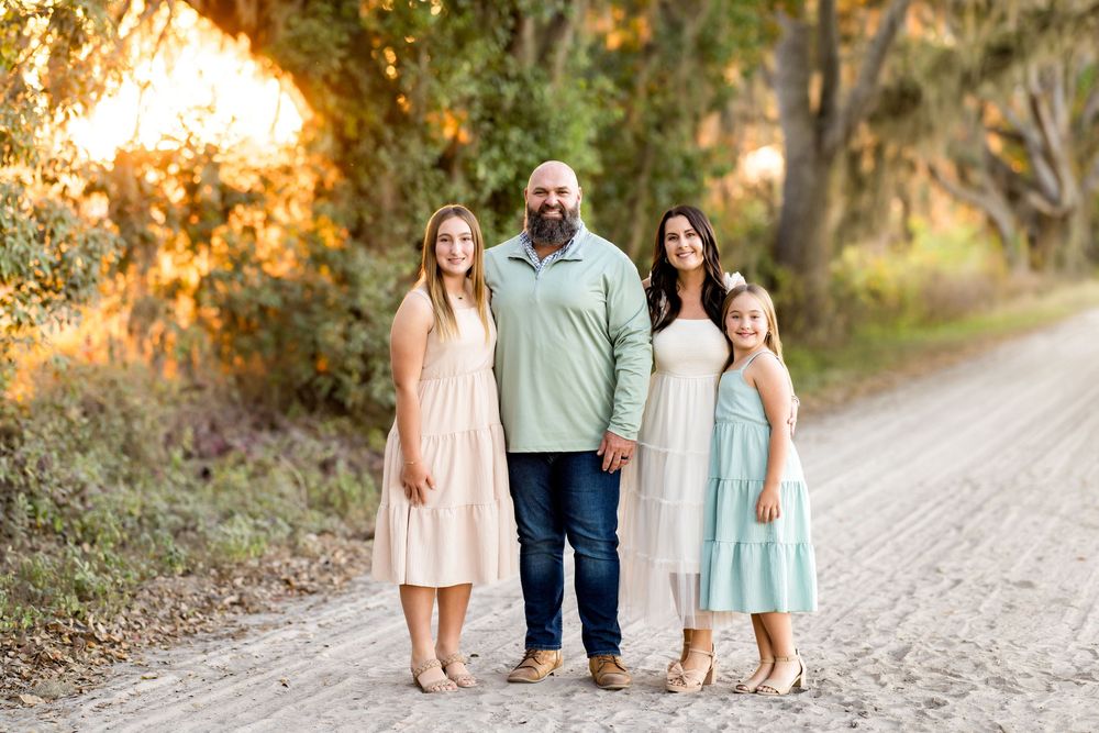 A group of people walk together on a sunlit dirt path through trees during golden hour.