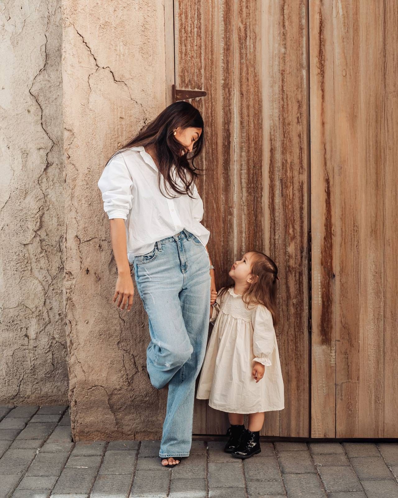 Mother and daughter in white casual outfits posing against warm golden curtain backdrop