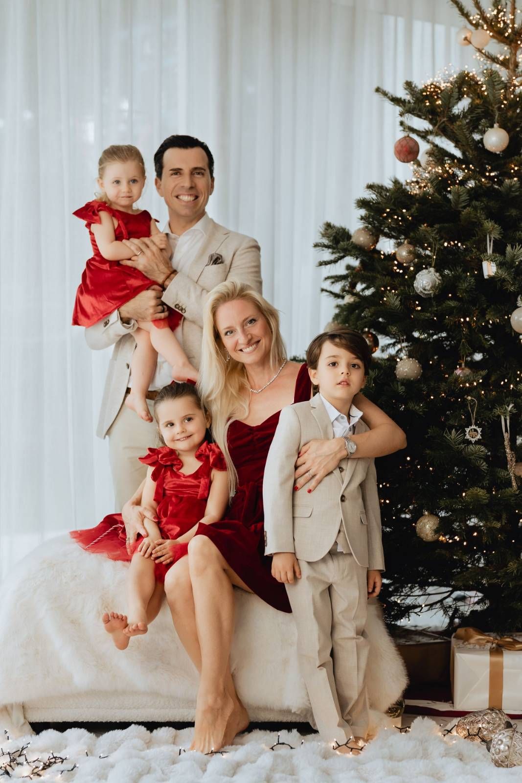 Family in red holiday outfits posing together with decorated Christmas tree indoors