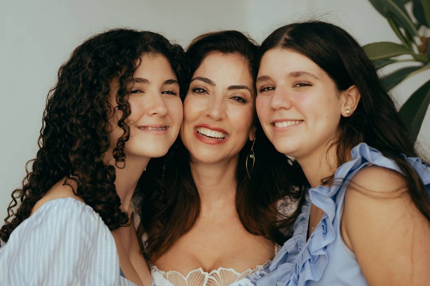 Three young women with long curly hair smiling together in casual indoor portrait