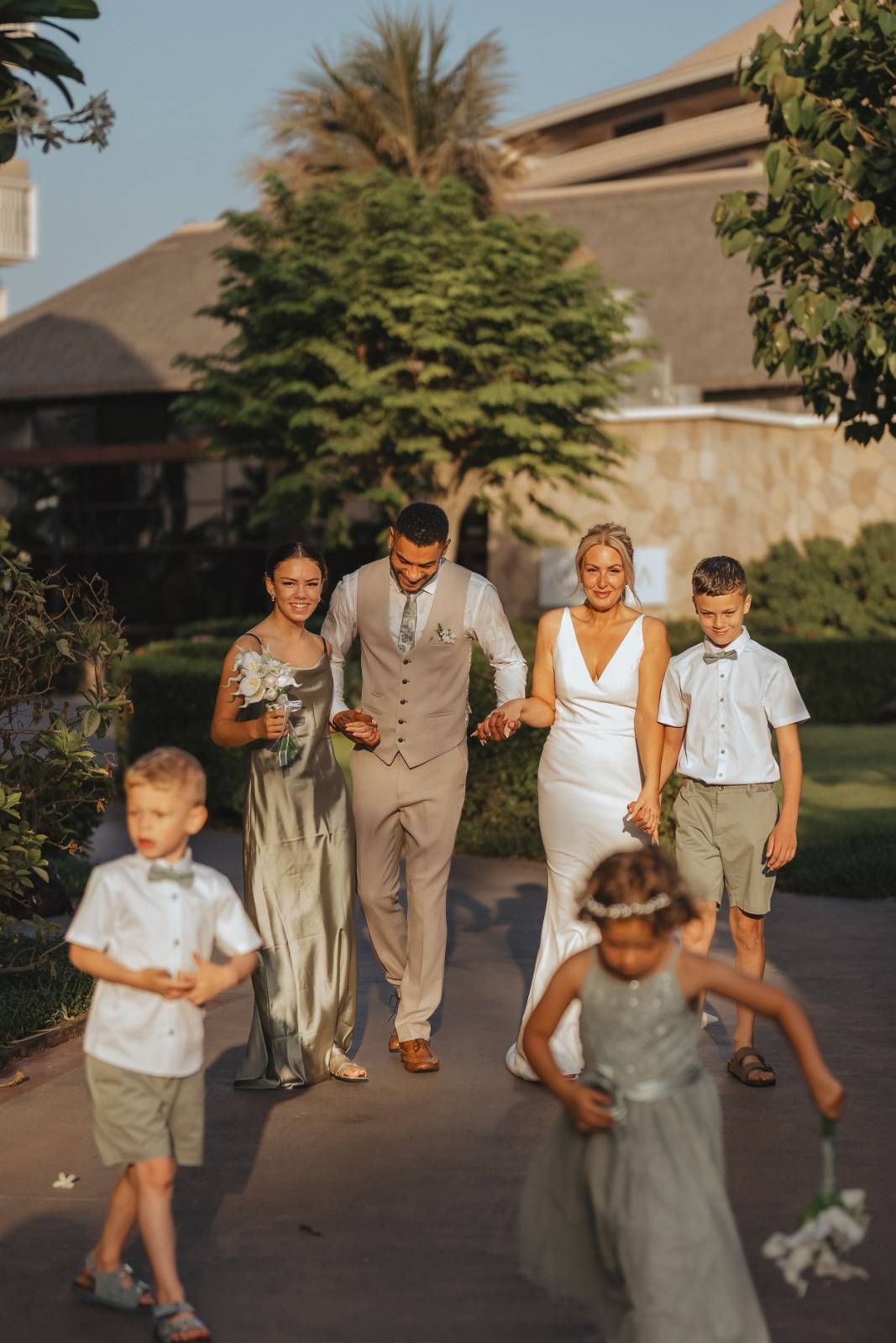 Extended family group in white and beige outfits posing outdoors under large palm tree in Dubai