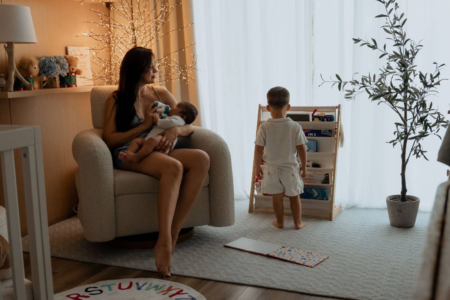 Mother in white shirt holding and playing with baby on bed near window