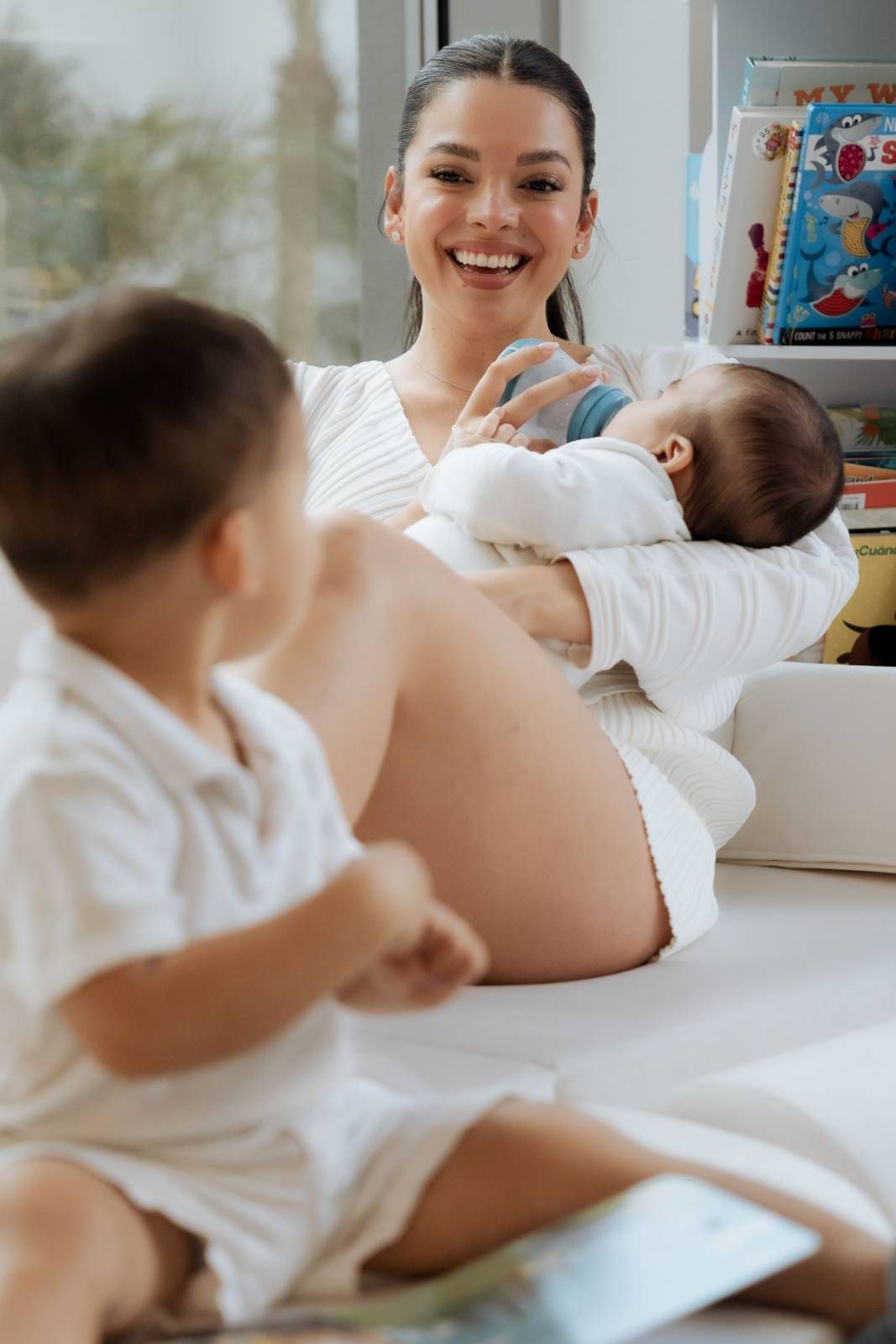 Mother in white shirt gently holding and kissing baby indoors