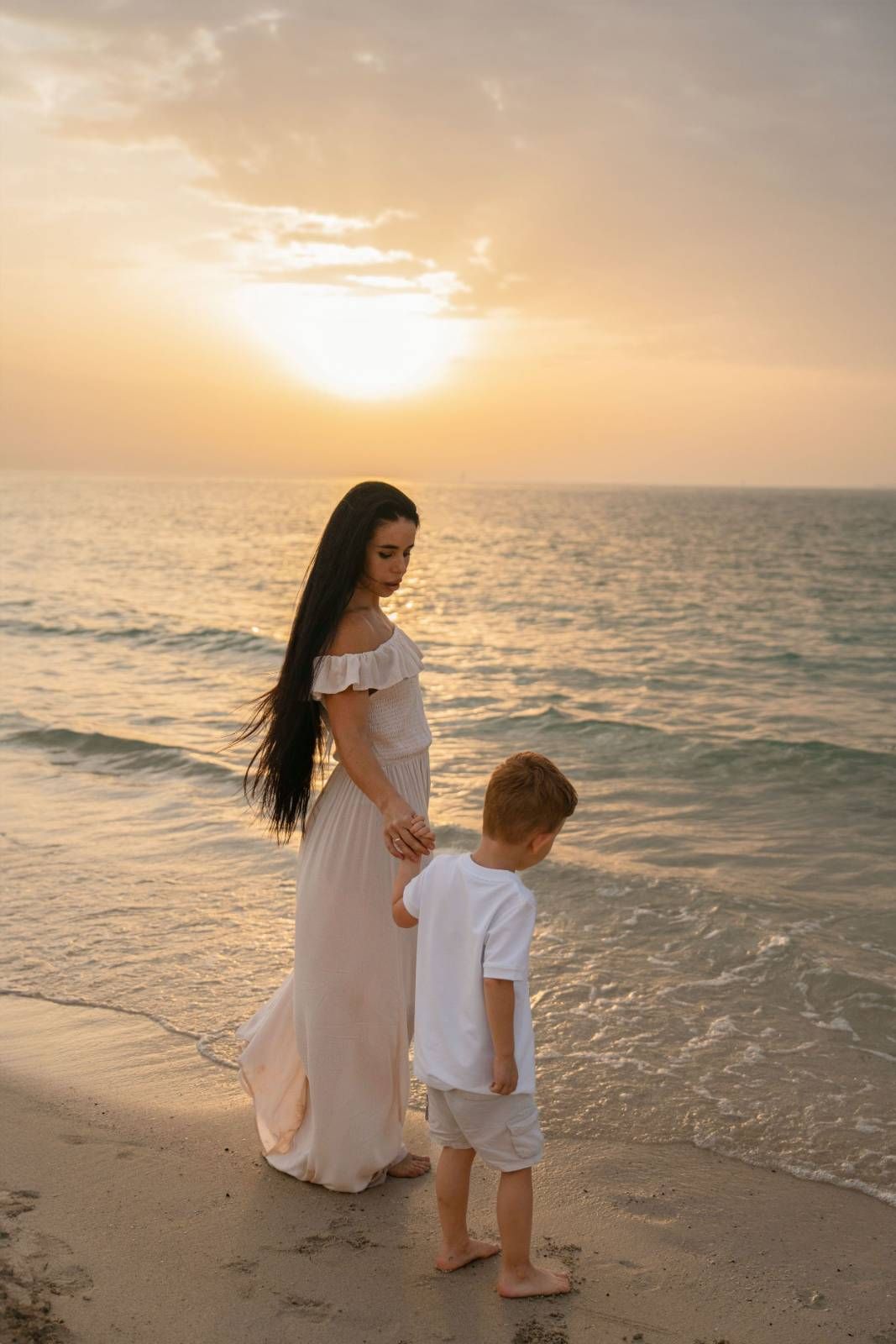 Woman standing on sandy beach in white outfit during golden hour sunset photography
