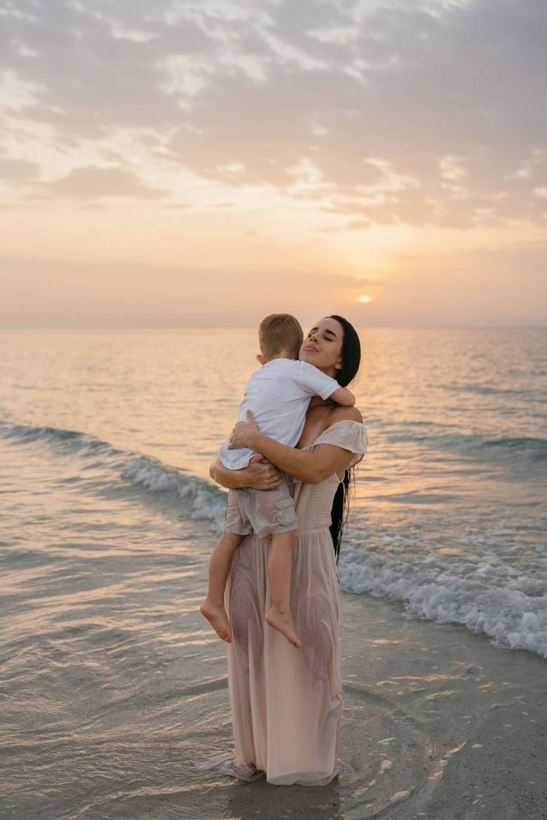 Woman holding child during golden sunset beach photography session by sea